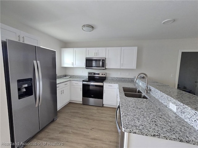 kitchen with white cabinetry, a sink, appliances with stainless steel finishes, light stone countertops, and a peninsula