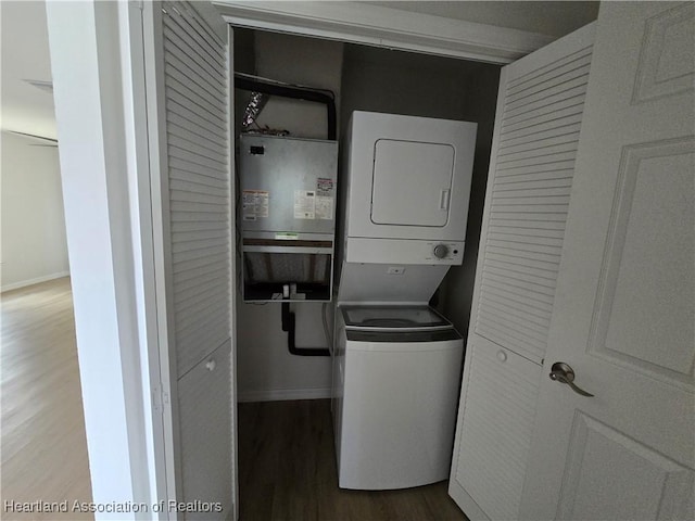 laundry room featuring stacked washer / drying machine, wood finished floors, baseboards, and laundry area