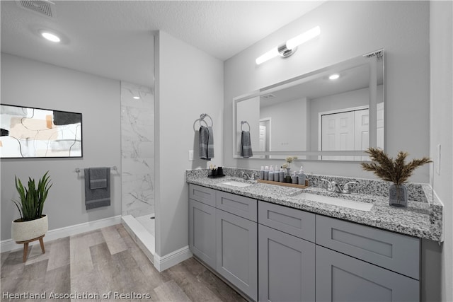 bathroom with hardwood / wood-style floors, vanity, a tile shower, and a textured ceiling