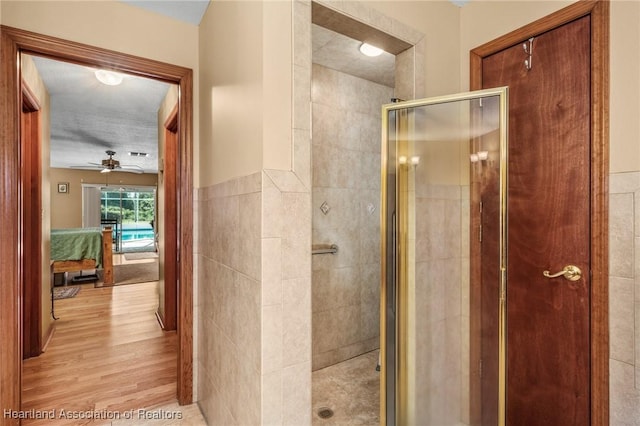 bathroom featuring ceiling fan, a shower with shower door, tile walls, and hardwood / wood-style flooring