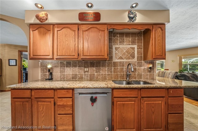 kitchen featuring tasteful backsplash, light stone counters, dishwasher, and sink