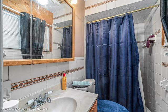 bathroom with curtained shower, vanity, tile walls, and toilet