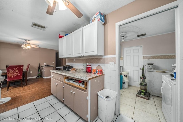 kitchen with tile walls, white cabinets, washer and dryer, and light tile patterned floors