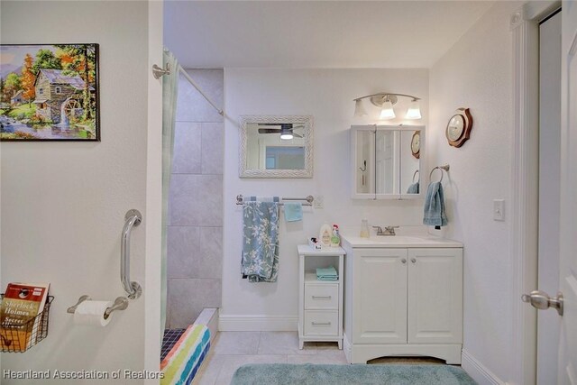 full bathroom with vanity, baseboards, tiled shower, and tile patterned floors