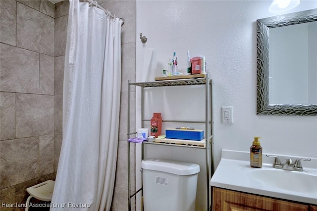 bathroom featuring toilet, tiled shower, and vanity