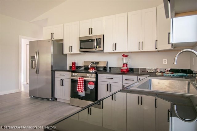 kitchen featuring dark countertops, lofted ceiling, stainless steel appliances, white cabinetry, and a sink