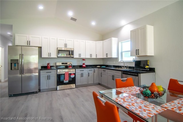 kitchen with light wood-style flooring, a sink, dark countertops, stainless steel appliances, and vaulted ceiling