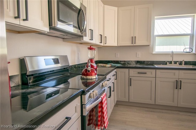 kitchen featuring a sink, stainless steel appliances, white cabinetry, dark countertops, and light wood-type flooring