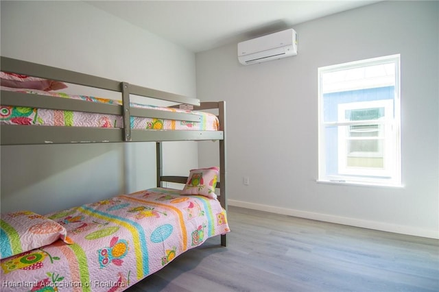 bedroom with baseboards, wood finished floors, and a wall unit AC