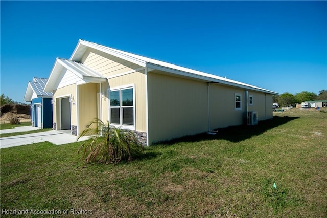 view of side of home with cooling unit, driveway, a yard, a garage, and metal roof