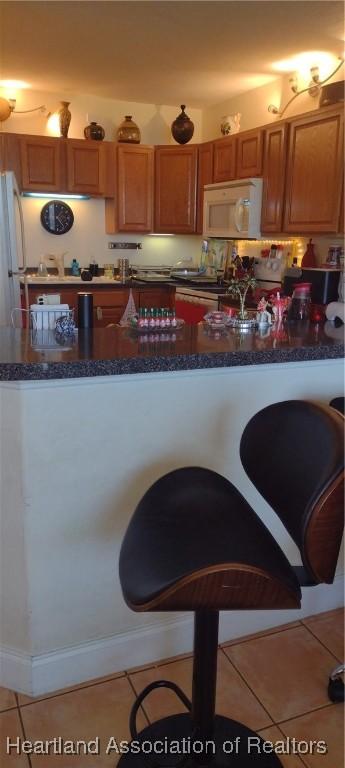 kitchen with tile patterned flooring, white appliances, and dark countertops