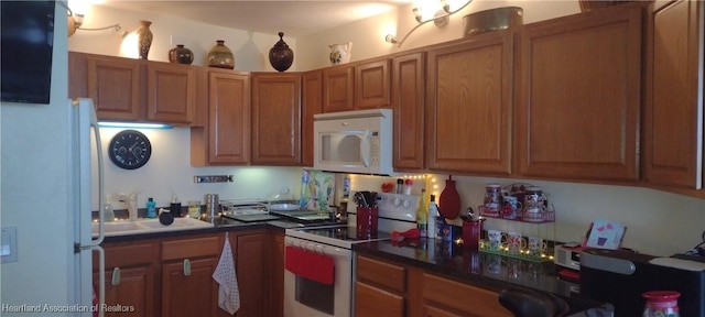 kitchen with a sink, white appliances, dark countertops, and brown cabinets