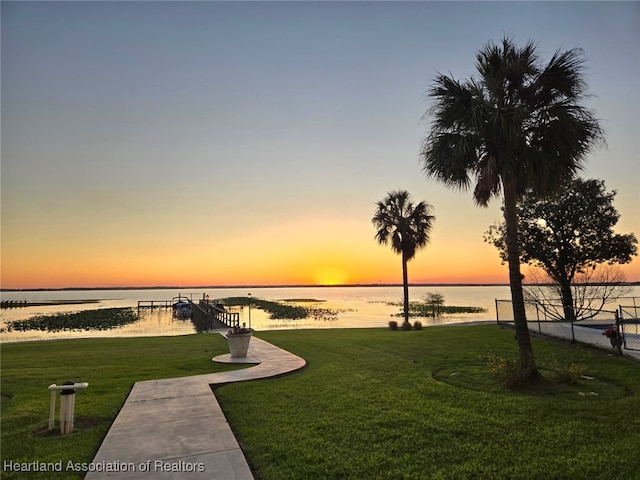 yard at dusk featuring a water view and fence