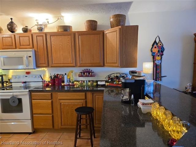 kitchen featuring light tile patterned flooring, white appliances, and brown cabinetry