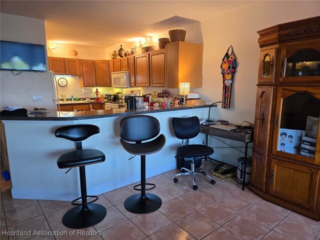 2131 Lakeview Dr Unit 106, Sebring, FL 33870 - kitchen with white microwave, dark countertops, a breakfast bar area, a peninsula, and brown cabinetry