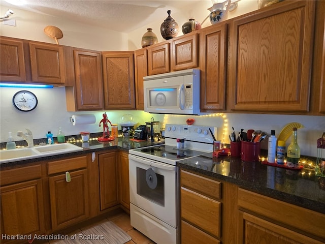2131 Lakeview Dr Unit 106, Sebring, FL 33870 - kitchen featuring white appliances, a sink, brown cabinetry, light tile patterned floors, and dark stone counters
