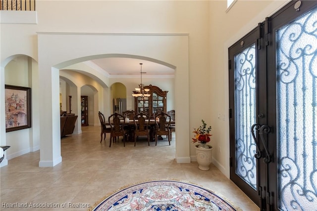 foyer entrance featuring light tile patterned flooring, ornamental molding, french doors, and an inviting chandelier