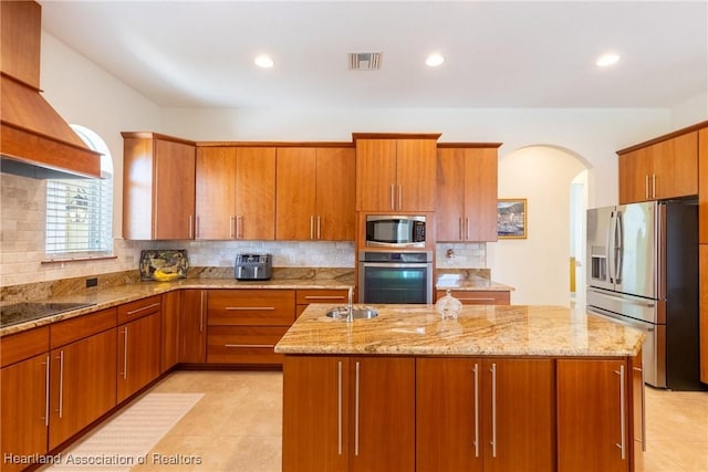 kitchen with decorative backsplash, appliances with stainless steel finishes, light stone countertops, and a kitchen island with sink