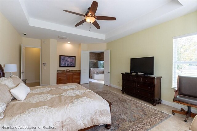 tiled bedroom featuring a tray ceiling, ensuite bath, and ceiling fan