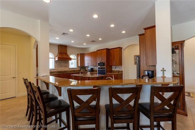 kitchen featuring kitchen peninsula, light tile patterned floors, custom range hood, and appliances with stainless steel finishes