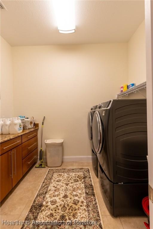 clothes washing area with washer and dryer, cabinets, and light tile patterned floors