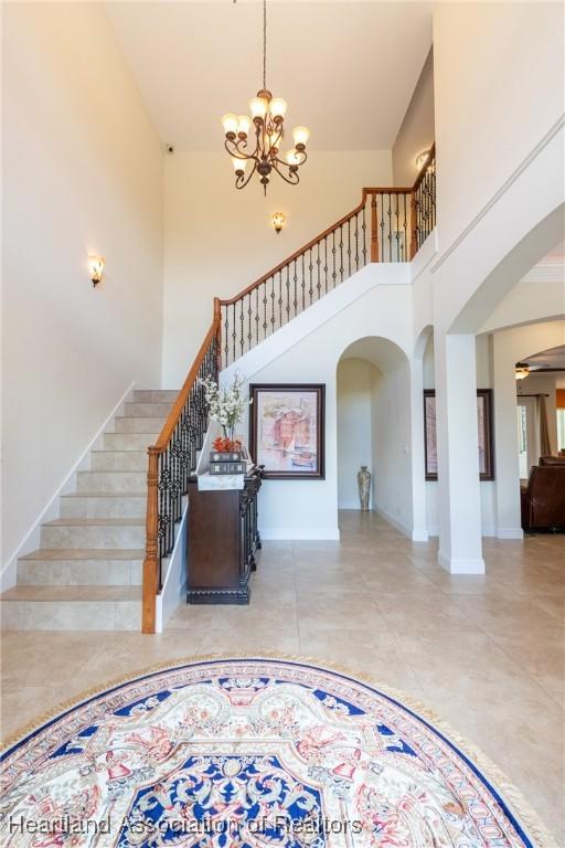 entryway featuring light tile patterned floors, a towering ceiling, and ceiling fan with notable chandelier