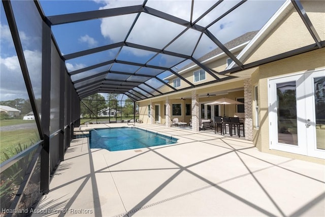 view of swimming pool with glass enclosure, ceiling fan, a patio area, and an outdoor bar