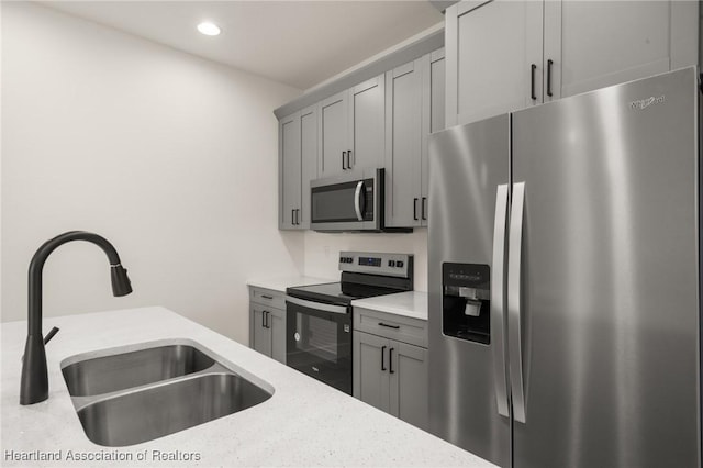 kitchen with appliances with stainless steel finishes, a sink, gray cabinets, recessed lighting, and light stone countertops