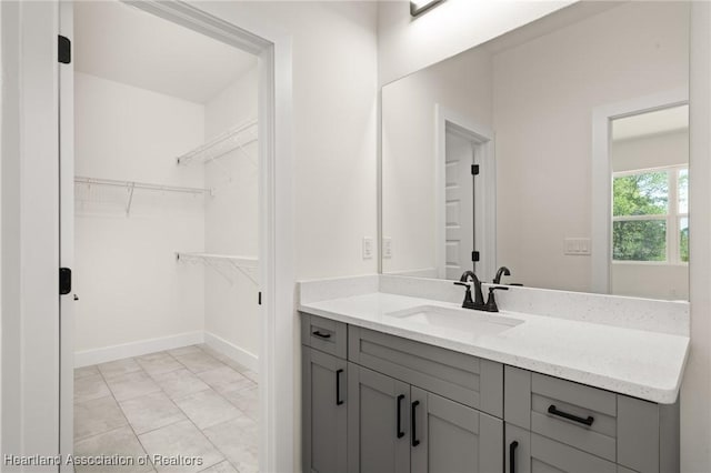 bathroom featuring a walk in closet, vanity, baseboards, and marble finish floors