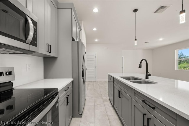 kitchen featuring appliances with stainless steel finishes, a sink, gray cabinetry, light stone countertops, and recessed lighting