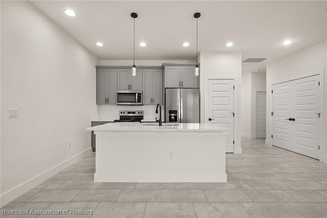 kitchen with appliances with stainless steel finishes, gray cabinetry, light countertops, a kitchen island with sink, and recessed lighting