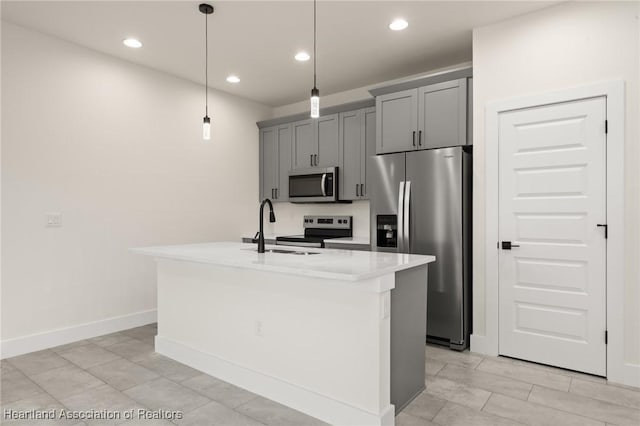 kitchen featuring stainless steel appliances, a sink, a kitchen island with sink, gray cabinetry, and light countertops
