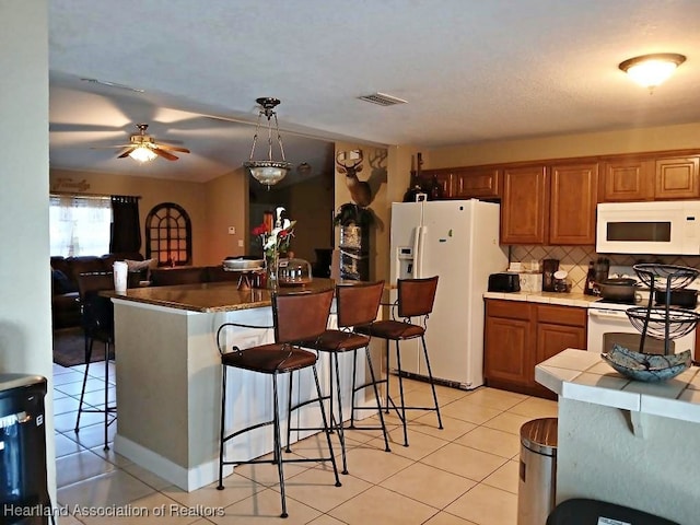 kitchen with white appliances, light tile patterned floors, a kitchen bar, backsplash, and visible vents
