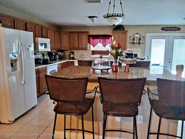 kitchen with light tile patterned flooring, tasteful backsplash, white appliances, a center island, and a kitchen bar