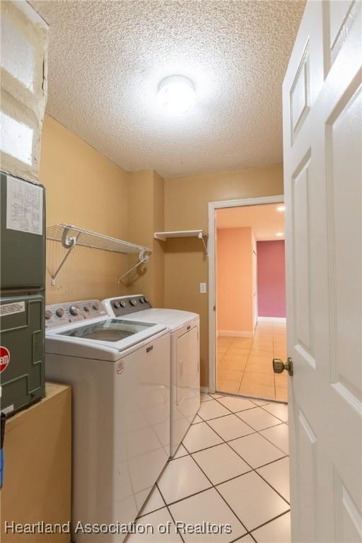 laundry room featuring washing machine and clothes dryer, a textured ceiling, and light tile patterned floors