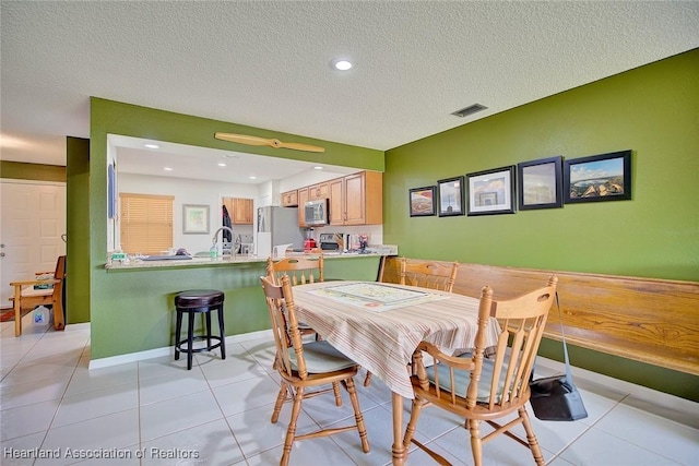 dining space with sink, a textured ceiling, and light tile patterned floors