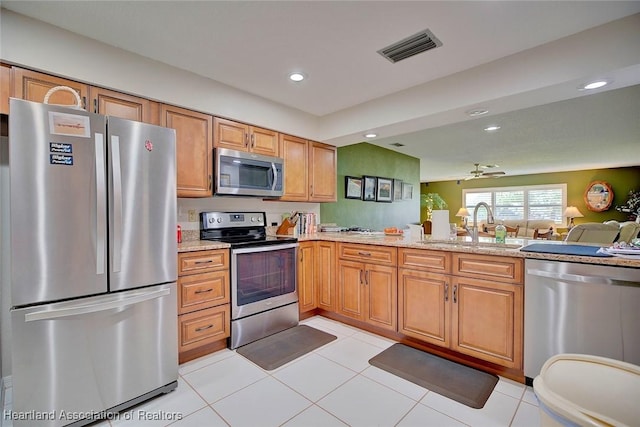 kitchen with light tile patterned flooring, appliances with stainless steel finishes, light stone countertops, and sink