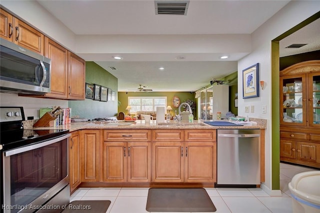 kitchen with appliances with stainless steel finishes, kitchen peninsula, sink, and light tile patterned floors