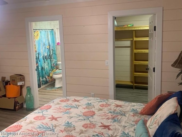 bedroom with a closet, connected bathroom, wood finished floors, and wooden walls