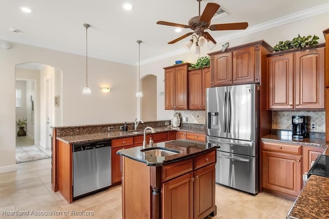 kitchen featuring decorative light fixtures, tasteful backsplash, stainless steel appliances, crown molding, and a center island with sink