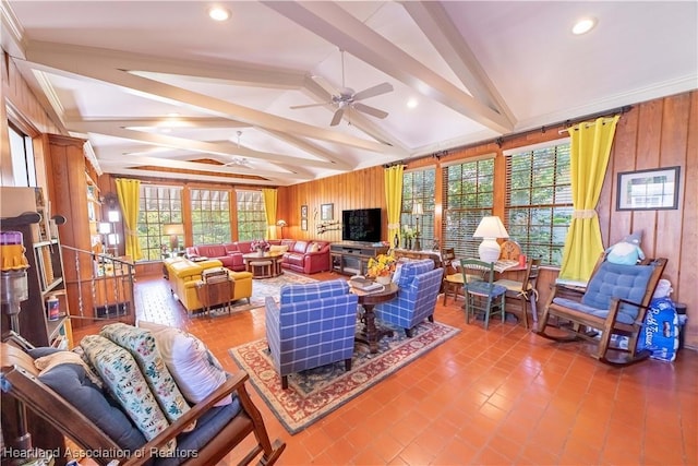 tiled living room with a wealth of natural light, vaulted ceiling with beams, ceiling fan, and wooden walls