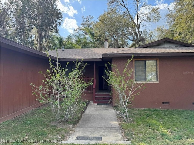 entrance to property featuring stucco siding, a lawn, roof with shingles, and crawl space