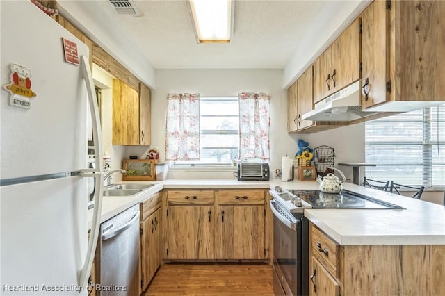 kitchen with a textured ceiling, light wood-type flooring, stainless steel appliances, and sink