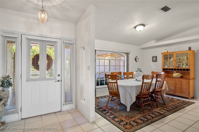 dining space with lofted ceiling, light tile patterned floors, a textured ceiling, and visible vents