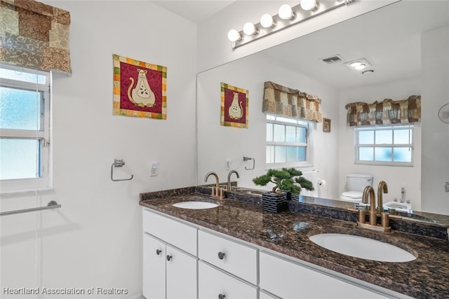 full bathroom featuring visible vents, a sink, toilet, and double vanity