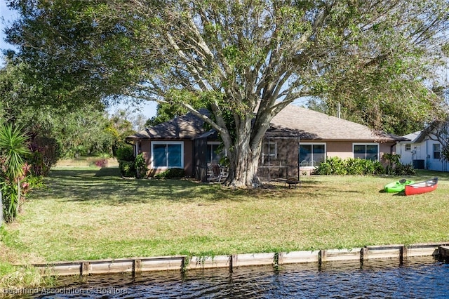 rear view of property with a yard, a water view, and stucco siding