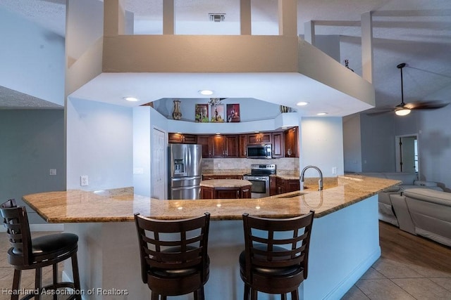 kitchen with kitchen peninsula, appliances with stainless steel finishes, a kitchen bar, tasteful backsplash, and sink