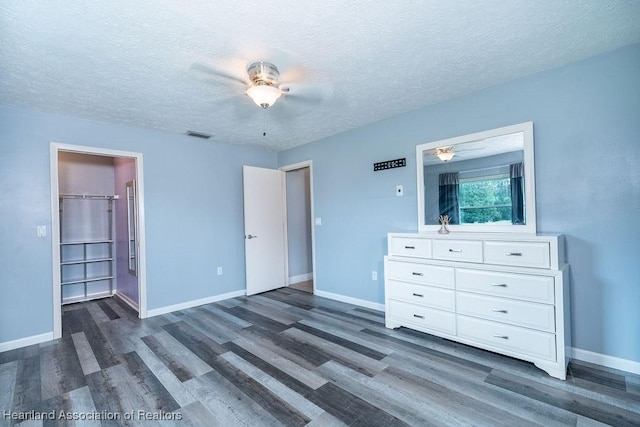 unfurnished bedroom with dark hardwood / wood-style flooring, a walk in closet, a textured ceiling, and a closet