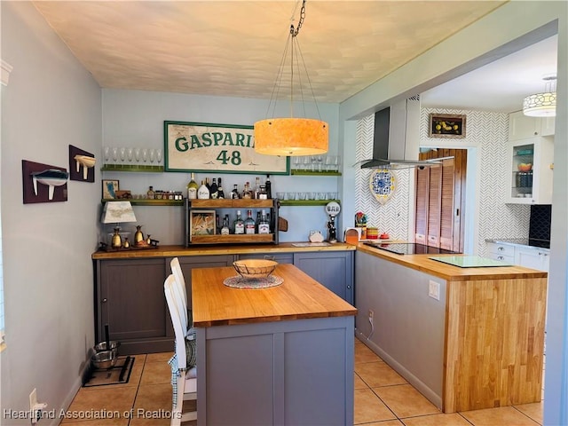 interior space featuring a center island, wall chimney exhaust hood, pendant lighting, and wood counters