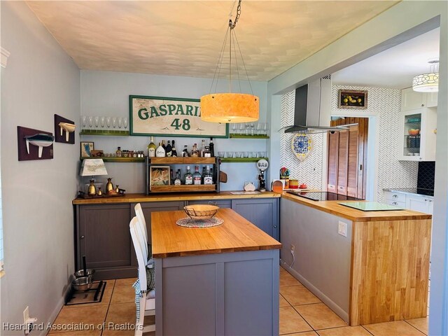 kitchen featuring pendant lighting, butcher block countertops, a kitchen island, and wall chimney range hood